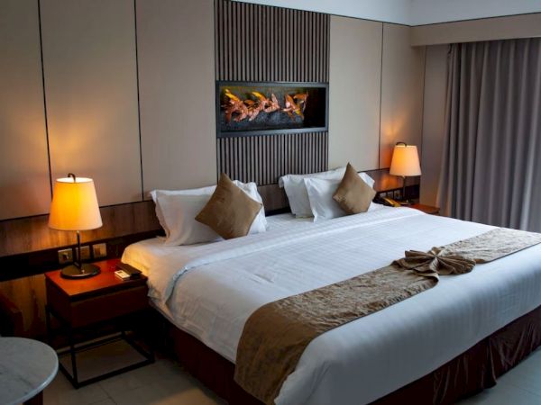 A modern hotel room with a large bed, decorative pillows, bedside lamps, and wall art, creating a cozy and inviting atmosphere.