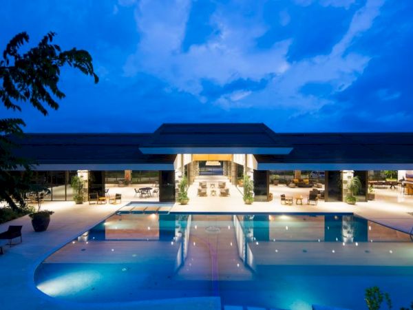 A modern building with a large illuminated pool in the foreground, set against a deep blue evening sky.