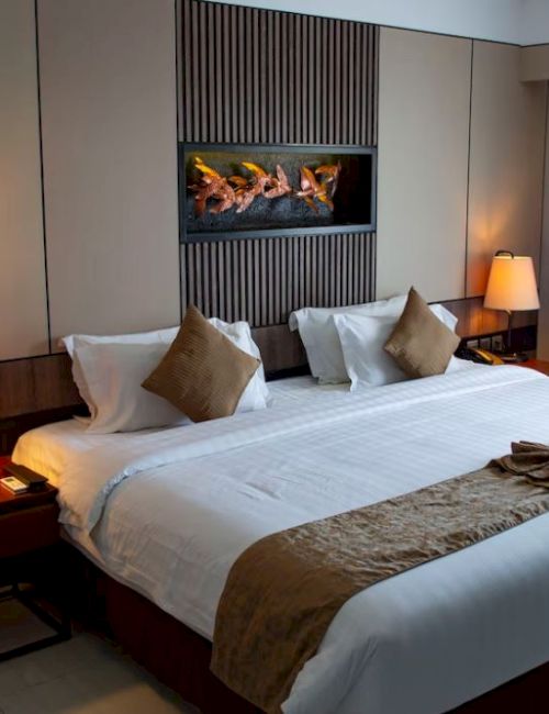 A cozy hotel room features a large bed with decorative pillows, bedside tables with lamps, wall art, and curtains by a window.