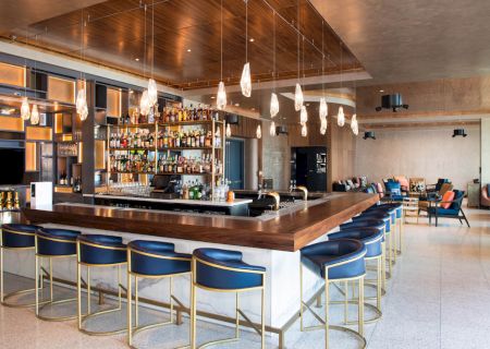 A modern bar with stylish seating, a well-stocked liquor display, and elegant lighting, adjacent to a cozy seating area.