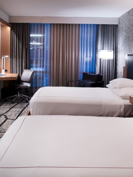 A modern hotel room with two beds, a TV, desk, and lamps; features a stylish design with wood and patterned elements.