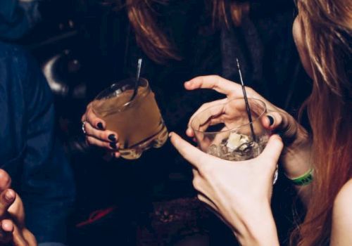 People are socializing, holding drinks and laughing in a dim setting.
