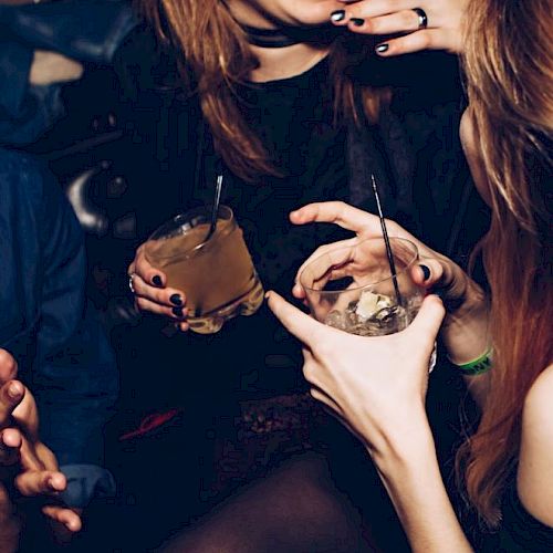 People are socializing, holding drinks and laughing in a dim setting.