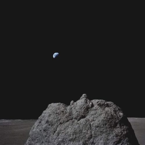 A view of Earth from the Moon, showing a large rock in the foreground and Earth in the distance against a dark space backdrop.