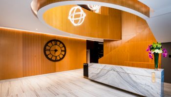 Modern lobby with a marble counter, large wall clock, spiral staircase, and decorative lights.