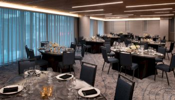 A banquet hall with round tables set for an event, featuring elegant tableware, black napkins, and centerpieces under ambient lighting.