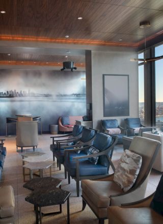 A modern lounge with leather chairs, a mural, and large windows offering a view of a bay and distant city skyline.