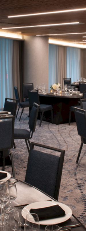 The image shows a banquet hall set up with round tables, elegant place settings, and subdued lighting ready for an event.