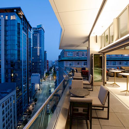 A modern rooftop terrace overlooks a cityscape with tall buildings, featuring outdoor seating and large windows.