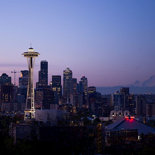 Seattle skyline at dusk with the Space Needle and Mount Rainier in the background, city lights illuminating the scene.