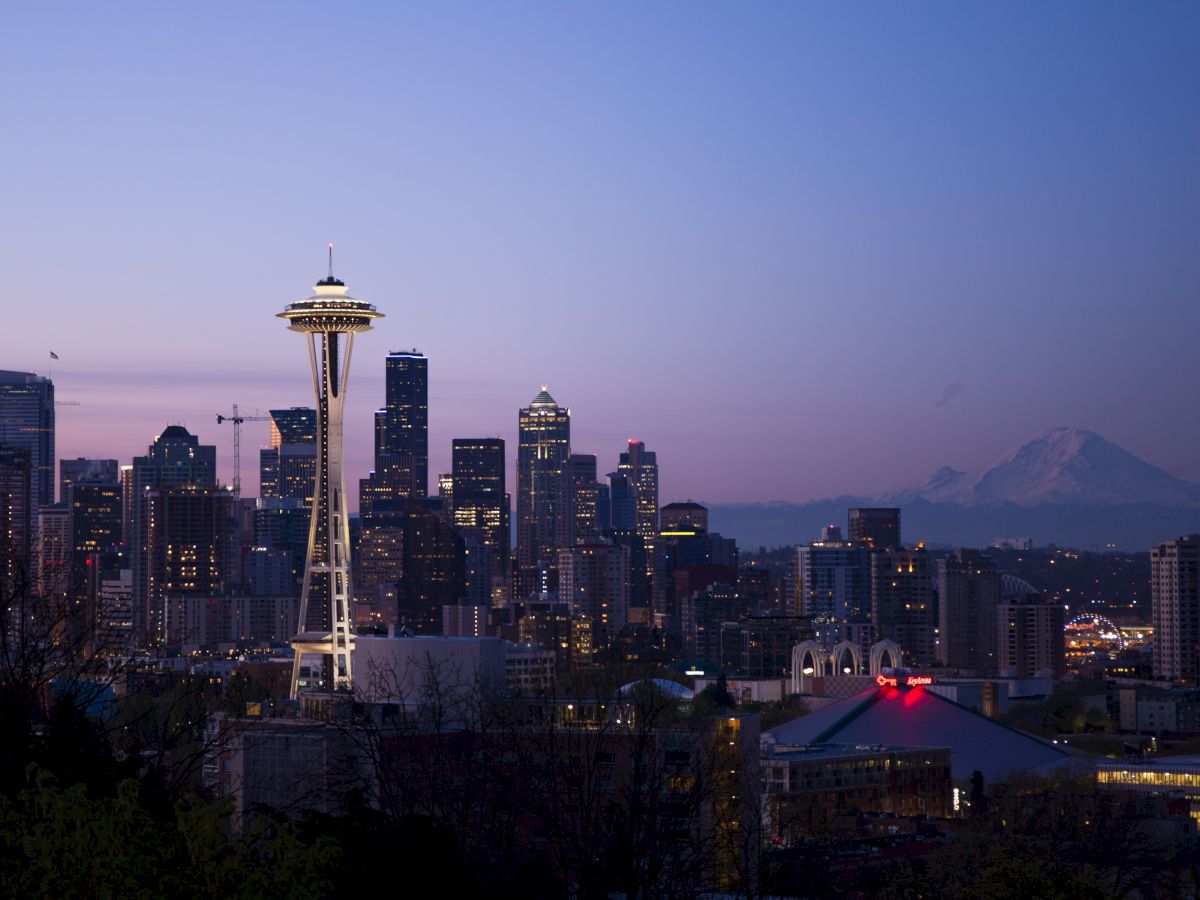 A twilight view of Seattle's skyline featuring the Space Needle, silhouetted buildings, and Mount Rainier in the background.