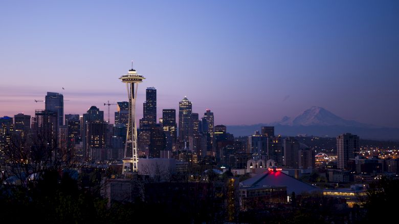 A twilight view of Seattle's skyline featuring the Space Needle, silhouetted buildings, and Mount Rainier in the background.