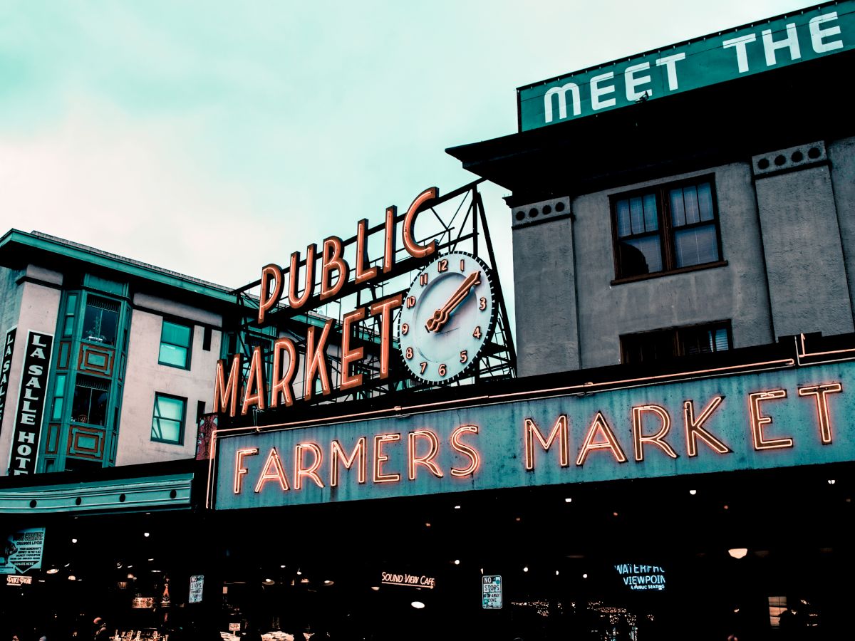 The image shows the iconic Public Market and Farmers Market sign with a clock, located in an urban setting with surrounding buildings.