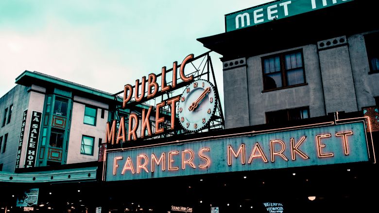 The image shows the iconic Public Market and Farmers Market sign with a clock, located in an urban setting with surrounding buildings.
